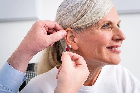 Ältere Frau bekommt ein modernes Hörgerät eingesetzt, Hörhilfe und Hörakustiker Beratung.